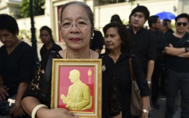 Une femme tient une représentation du Roi thaïlandais Bhumibol Adulyadej, dans la queue pour rendre hommage au Grand Palais à Bangkok le 14 octobre 2016 (Crédits : AFP/Munir Uz Zaman)