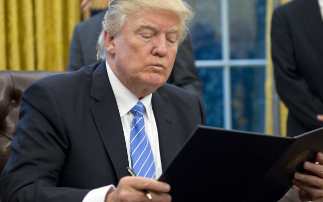 Le président américain Donald Trump signant son premier décret exécutif dans le Bureau ovale, le 23 janvier 2017. (Crédit : Ron Sachs/Pool/Getty Images)