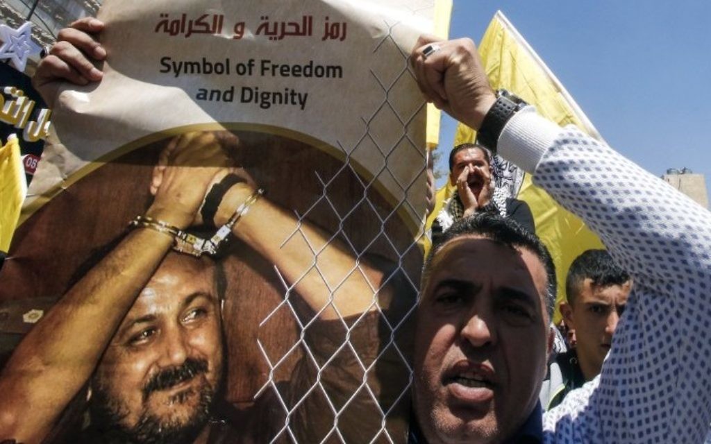 Un homme avec une photo du terroriste palestinien condamné Marwan Barghouthi pour demander sa libération pendant une manifestation de soutien aux détenus en grève de la faim à Hébron, en Cisjordanie, le 17 avril 2017. (Crédit : Hazem Bader/AFP)