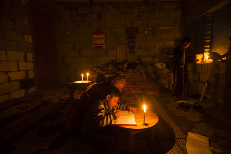 Une Palestinienne aide son fils à faire ses devoirs à la lumière des bougies, alors qu'une crise électrique touche la bande de Gaza, dans le camp de réfugiés de Khan Yunis, le 19 avril 2017. (Crédit : Mahmud Hams/AFP)