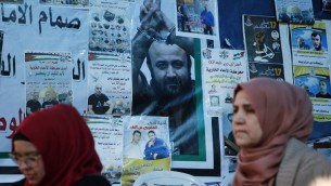 Des Palestiniennes devant un mur d'affiches, dont un portrait de Marwan Barghouthi, pendant un rassemblement de soutien aux prisonniers palestiniens en grève de la faim, à Ramallah, en Cisjordanie, le 24 avril 2017. (Crédit : Abbas Momani/AFP)