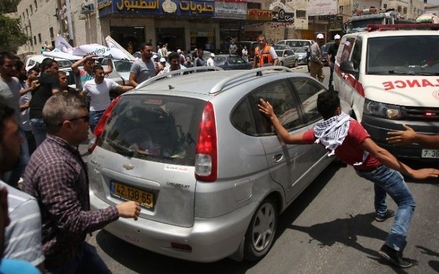 Des manifestants palestiniens encerclent la voiture d'un Israélien qui se fraye un chemin parmi la foule, près du checkpoint d'Hawara, en Cisjordannie, le 18 mai 2017. (Crédit : Jaafar Ashtiyeh/AFP)