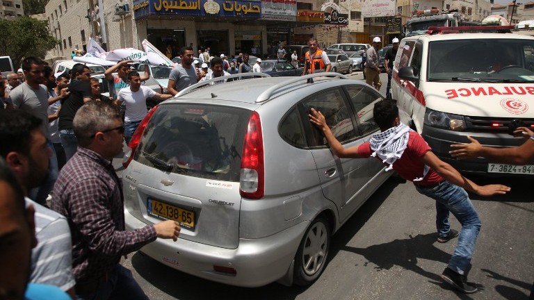 Des manifestants palestiniens encerclent la voiture d'un Israélien qui se fraye un chemin parmi la foule, près du checkpoint d'Hawar, en Cisjordannie, le 18 mai 2017. (Crédit : AFP Photo / Jaafar Ashtiyeh) 