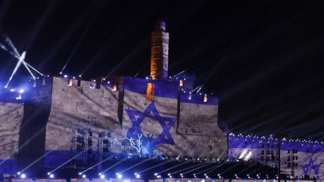 Les gens regardent une projection du drapeau israélien au cours d'un spectacle de son et lumière projeté sur les murs de la Vieille ville de Jérusalem pour célébrer le début de la semaine du 50ème anniversaire de la guerre israélo-arabe de 1967, le 20 mai 2017 (Crédit : GALI TIBBON / AFP PHOTO)