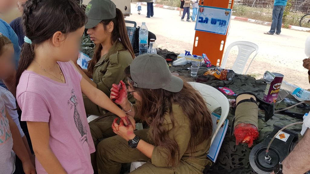 Des soldats de la brigade Etzion dessinent de fausses blessures d'éclats d'obus aux enfants de l'implantation de Tekoa pendant une exposition militaire pour Yom HaAtsmaout, le 2 mai 2017. (Crédit : autorisation)