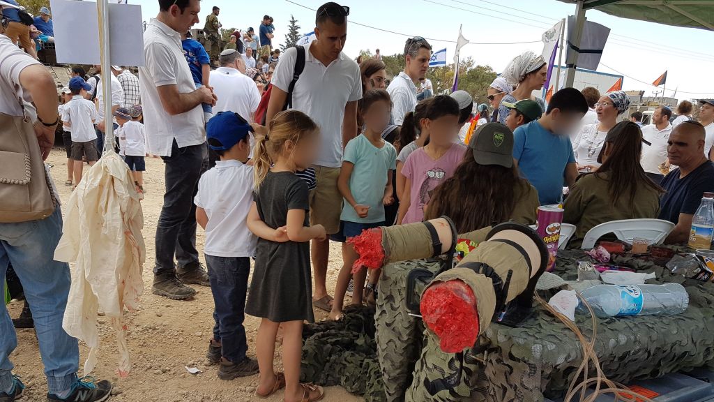 Des soldats de la brigade Etzion dessinent de fausses blessures d'éclats d'obus devant une paire de fausses jambes amputées aux enfants de l'implantation de Tekoa pendant une exposition militaire pour Yom HaAtsmaout, le 2 mai 2017. (Crédit : autorisation)