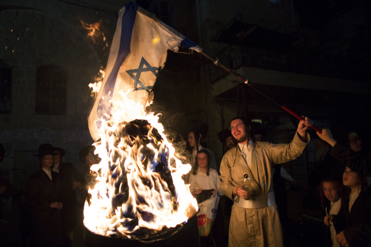 Un membre de la secte anti-sioniste Neturei Karta brûle un drapeau israélien pendant la fête de Lag BaOmer, dans le quartier ultra-orthodoxe de Mea Shearim, à Jérusalem, en mai 2014. (Crédit : Yonatan Sindel/Flash90)