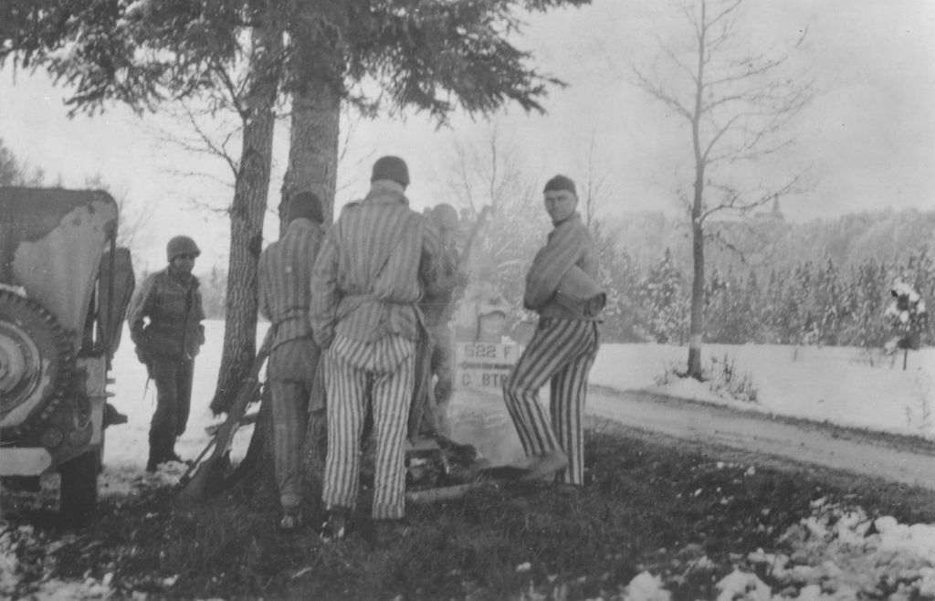 Les survivants d'une marche de la mort à Dachau blottis autour d'un feu de camp préparé par les soldats nippo-américains du 522ème Régiment d'infanterie. Le soldat sur la gauche est George Oiye. (Autorisation : USHMM/Eric Saul)