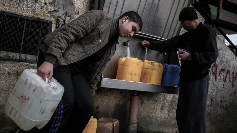 Des Palestiniens remplissent des bouteilles et des jerricanes d'eau potable à des robinets publics au camp de réfugiés de Rafah dans le sud de la bande de Gaza, le 22 février 2017 (Crédit : Said Khatib/AFP)