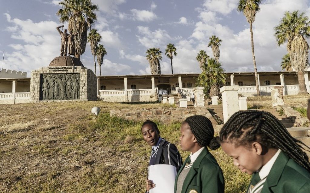 Des écolières namibiennes passent devant le mémorial construit en hommage aux victimes du génocide présumé commis par les forces allemandes des tribus Herero et Nama en 1904, le 20 juin 2017 à Windhoek, en Namibie (Crédit : AFP PHOTO / GIANLUIGI GUERCIA)