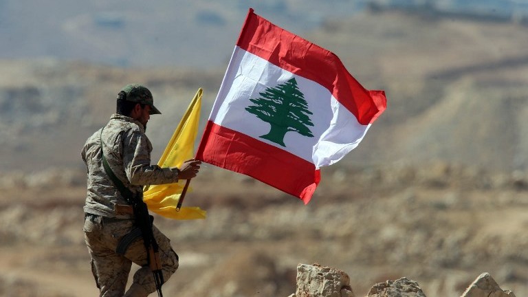 Un membre du groupe terroriste du Hezbollah tient des drapeaux libanais et du  Hezbollah durant une visite organisée pour la presse à côté de la ville frontalière d'Arsal, le 25 juillet 2017 (Crédit : Stringer/AFP)