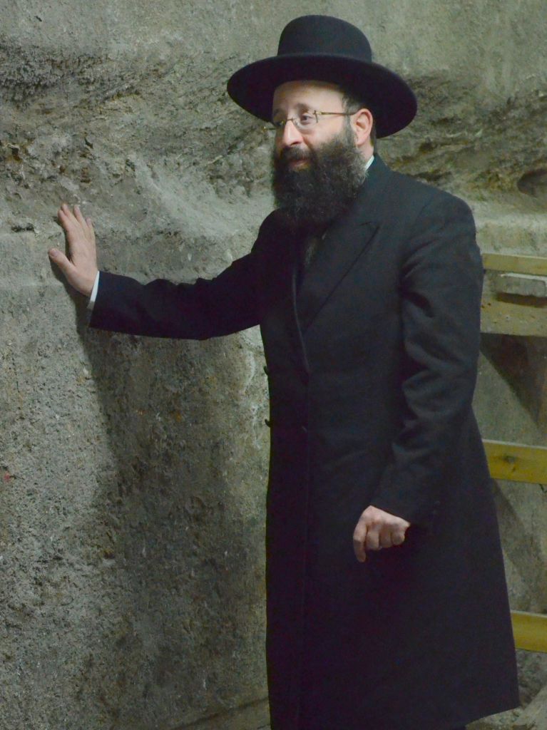 Le rabbin Shmuel Rabinovitch, rabbin du mur Occidental et des lieux saints, devant les pierres du mur Occidental découvertes pendant les fouilles sous l'Arche de Wilson, dans la Vieille Ville de Jérusalem, en octobre 2017. (Crédit : Yaniv Berman/Autorité israélienne des Antiquités)