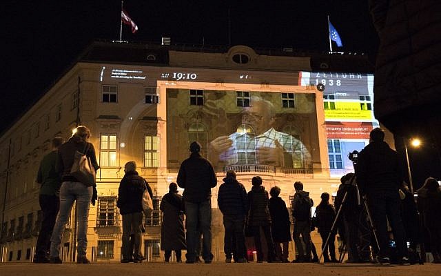 Les gens regardent 'Zeituhr 1938', une projection sur la façade de la chancellerie autrichienne qui retrace les moments obscurs menant à la prise par les nazis d'Adolf Hitler en 1938, un jour avant le 80ème anniversaire de l'annexion de l'Autriche ("Anschluss"), le 11 mars 2018 à Vienne en Autriche, le 11 mars 2018 (Crédit :  / AFP PHOTO / JOE KLAMAR)