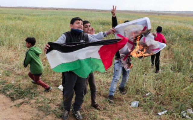 Des enfants de la bande de Gaza agitent un drapeau palestinien et brûle un drapeau à l'effigie de Donald Trump, le 30 mars 2018 (Crédit : Said Khatib/AFP)