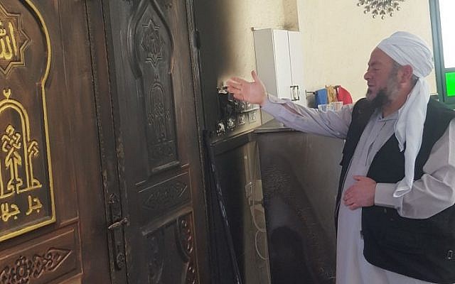 Un imam dans une mosquée du village palestinien d'Aqraba, dans le nord de la Cisjordanie, montre les dégâts causés par un incendie criminel survenu le 13 avril 2018. (Crédit : Zacharia Sadeh / Rabbis for Human Rights)