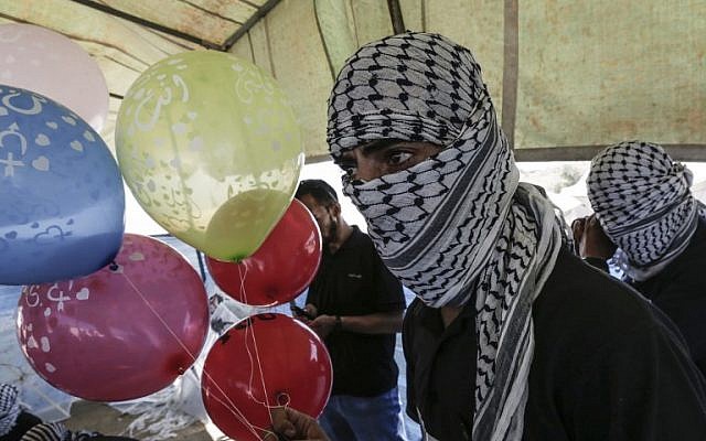 Des Palestiniens masqués préparent des ballons équipés de produits inflammables à envoyer en Israël depuis la bande de Gaza à al-Bureij, au centre de l'enclave, le 14 juin 2018 (Crédit :  / AFP PHOTO / MAHMUD HAMS