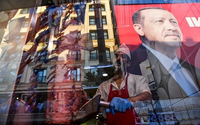 Tandis qu'un boucher tranche de la viande, l'on aperçoit le reflet d'un portrait du président turc Recep Tayyip Erdogan dans la fenêtre d'un restaurant turc sur la place Taksim d'Istanbul le 20 juin 2018. (Crédit : AFP / Bulent Kilic)