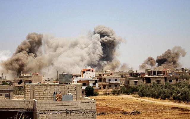 De la fumée émane des bâtiments durant une frappe des forces du régime syrien sur la ville de Busra al-Harir, à l'est de a province de Deraa, le 24 juin 2018. (Crédit : AFP/ Mohamad ABAZEED)