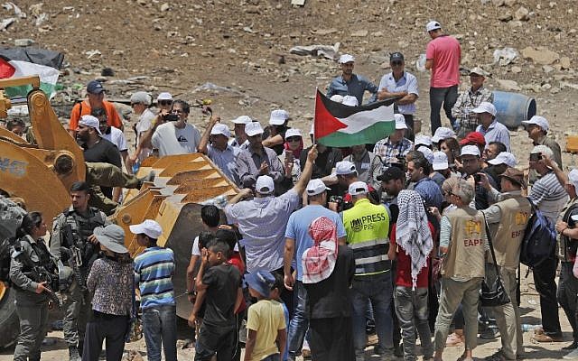 Des manifestants brandissent des drapeaux palestiniens alors qu'ils tentent d'empêcher un tracteur de paver une route d'accès au village bédouin de Khan al-Ahmar, en Cisjordanie, le 4 juillet 2018. (AFP Photo/Ahmad Gharabli)