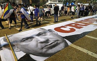 Une bannière avec un message politique et une photo du Premier ministre  Benjamin Netanyahu sur le sol alors que les membres de la communauté druze et leurs soutiens manifestent contre la loi sur l'Etat-nation à Tel Aviv, le 4 août 2018. Le message 
 est "Ministre du crime" (Crédit : AFP PHOTO / JACK GUEZ)