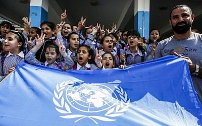Des écoliers palestiniens chantent des slogans et font le signe de la victoire devant le drapeau de l'ONU lors d'une manifestation organisée le 5 septembre 2018 dans le camp de réfugiés d'Arroub, près de Hébron, en Cisjordanie, dans une école financée par les États-Unis, qui a été construite sous les auspices de l'UNRWA. (Crédit : AFP PHOTO / HAZEM BADER)