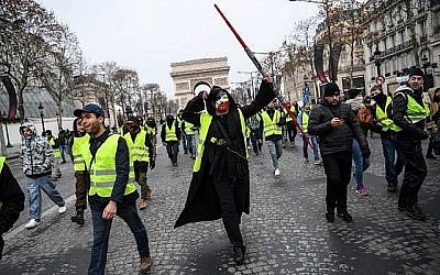 Un homme porte un masque d'Anonymous et un sabre laser de Jedi de Star wars durant les manifestations de gilets jaunes devant l'Arc de Triomphe à Paris, le 15 décembre 2018. (Crédit : Christophe Archambault/AFP)