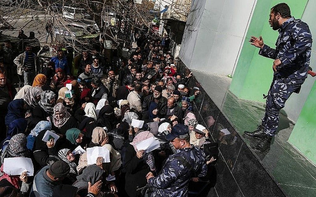Les forces de sécurité fidèles au Hamas organisent une file d'attente devant le bureau de poste central de la ville de Gaza le 26 janvier 2019, alors que les Palestiniens se rassemblent pour recevoir une aide financière du Qatar. (Crédit : Mahmud Hams/AFP)