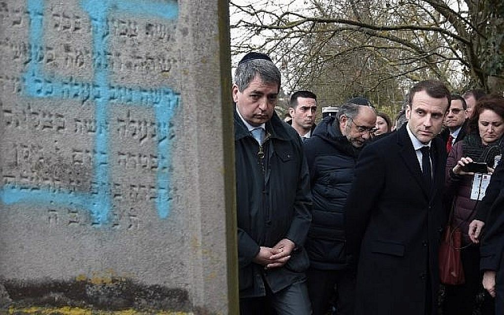 Le président français Emmanuel Macron observe une tombe vandalisée d'une croix gammée lors d'une visite au cimetière juif de Quatzenheim, le 19 février 2019, le jour des marches nationales contre la montée des attaques antisémites. (Frederick FLORIN / POOL / AFP)