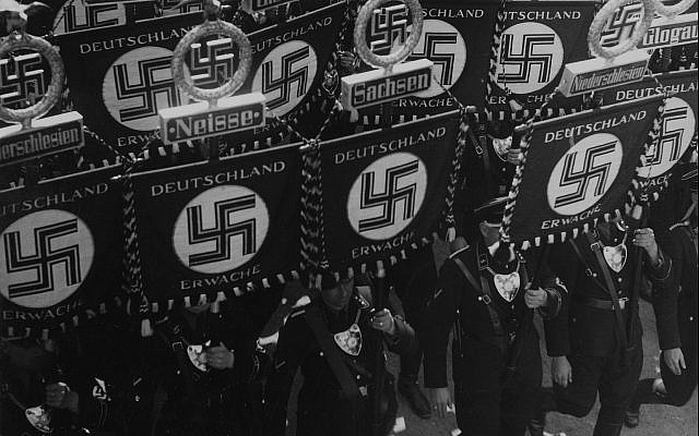 Des membres SS portent des drapeaux avec une croix gammées et des noms des régions et des villes allemandes alors qu'il marchent vers la mairie de Nuremberg, en Allemagne, le 10 septembre 1935, pour ouvrir la convention du Parti des Travailleurs d'Allemagne Nationale Socialiste (AP Photo).