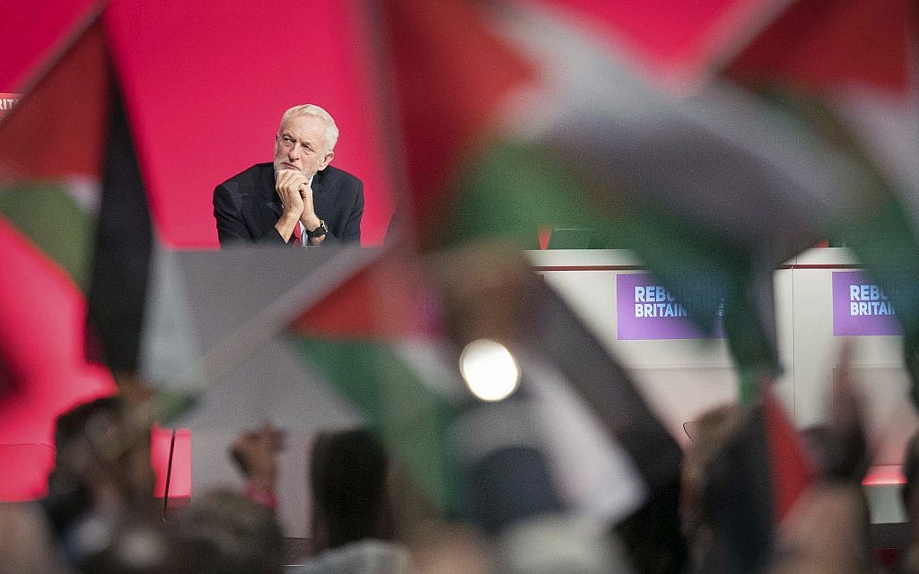 Le dirigeant du Parti travailliste britannique Jeremy Corbyn est assis sur la scène alors que ses partisans agitent des drapeaux palestiniens lors de la conférence annuelle du parti à Liverpool, en Angleterre, le 25 septembre 2018. (Stefan Rousseau/PA via AP)