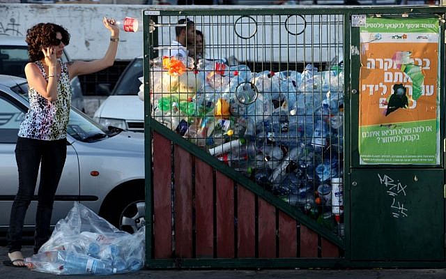 Une femme jette une bouteille dans un bac de recyclage du centre de Jérusalem. (Crédit photo : Nati Shohat/Flash90)
