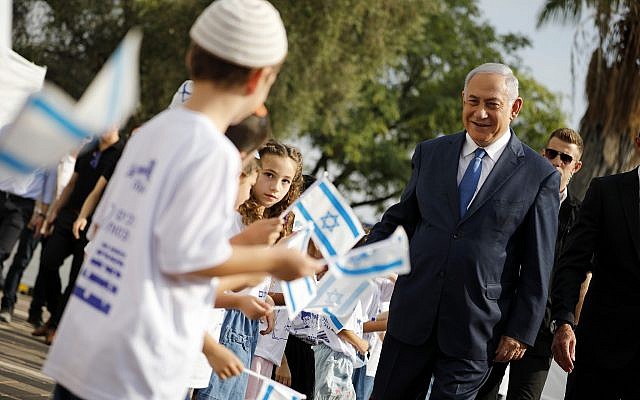 Le Premier ministre Benjamin Netanyahu, à droite, salue les élèves qui brandissent des drapeaux israéliens lors d'une cérémonie organisée lors de la rentrée scolaire dans l'implantation d'Elkana, en Cisjordanie, le 1er septembre (Crédit :  Amir Cohen/Pool Photo via AP)