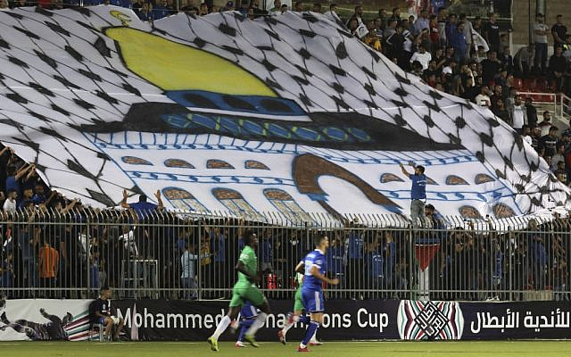 Des spectateurs tiennent un immese drapeau représentant le Dôme du Rocher, durant un match opposant l'équipe palestinienne à l'équipe marocaine, en Cisjordanie, le 3 octobre 2019. (Crédit : ABBAS MOMANI / AFP)