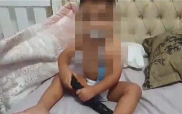 Un bébé de 18 mois filmé en train de jouer avec une arme dans son lit à Umm al-Fahm, dans le nord du pays (Capture d'écran : Kan)