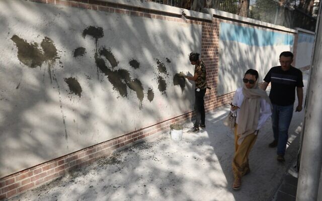 Des Iraniens passent devant une fresque partiellement recouverte de ciment sur le mur de l'ancienne ambassade américaine à Téhéran, le 29 septembre 2019. (Crédit : ATTA KENARE / AFP)