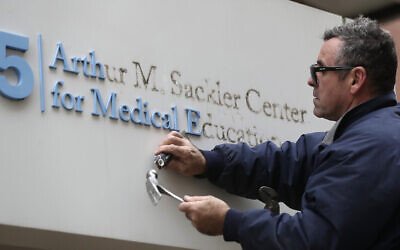 Gabe Ryan, un employé, supprime les lettres formant le nom d' Arthur M. Sackler à l'entrée du bâtiment de l'école de médecine Tufts à Boston, le 5 décembre 2019 (Crédit :  AP Photo/Steven Senne)