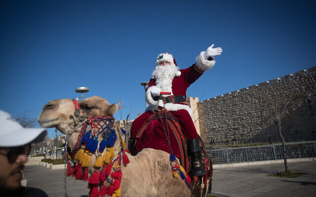 Un homme déguisé en Père Noël chevauche un chameau à la porte de Jaffa dans la Vieille Ville de Jérusalem, pendant la distribution d'arbres de Noël et quelques jours avant la prochaine fête de Noël, le 19 décembre 2019. (Yonatan Sindel/Flash90)