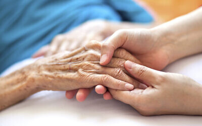 Illustration : Une femme tenant la main d'une femme âgée sur le lit. (Crédit :Pablo_K; iStock by Getty Images)