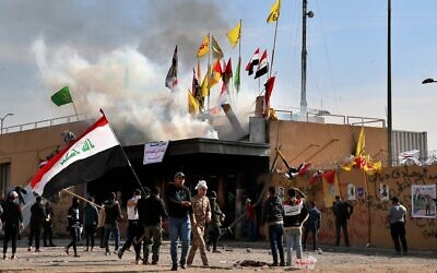 Des miliciens pro-iraniens et leurs partisans ont mis le feu tandis que des soldats américains tirent des gaz lacrymogènes lors d'un rassemblement devant l'ambassade des États-Unis à Bagdad, en Irak, le 1er janvier 2020. (Crédit : Khalid Mohammed / AP)
