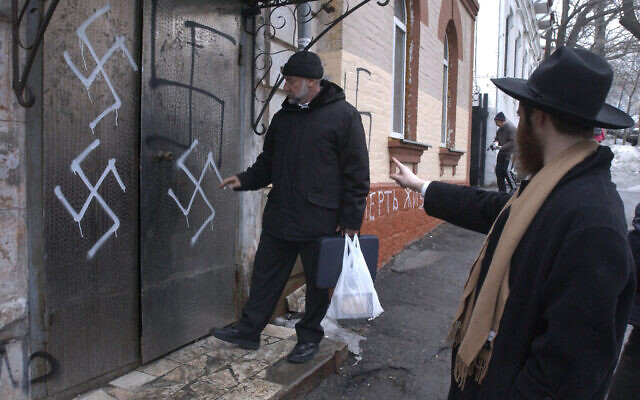Illustration :le chef de la communauté juive Gennady Klebanov, à gauche, est sur le point d'entrer par la porte de la synagogue taguée de croix gammées, que le rabbin en chef de Vladivostok Isroel Silberstain, à droite, montre du doit, au port russe d'Extrême-Orient de Vladivostok, le 2 mars 2007. (Crédit : AP)