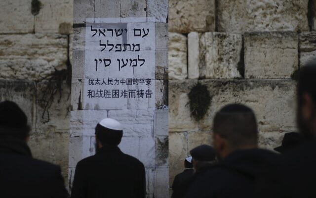 Des Juifs prient au mur Occidental, dans la Vieille Ville de Jérusalem, lors d'une prière pour les malades du coronavirus apparu en Chine. L'affiche dit "Le peuple d'Israël prie pour la Chine". Photo prise le 16 février 2020 (Crédit : Ariel Schalit/AP)