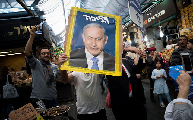 Un partisan du Likud tient une affiche de campagne montrant le Premier ministre  Benjamin Netanyahu sur le marché  Mahane Yehuda de Jérusalem, le 7 avril 2019 (Crédit : Yonatan Sindel/Flash90)