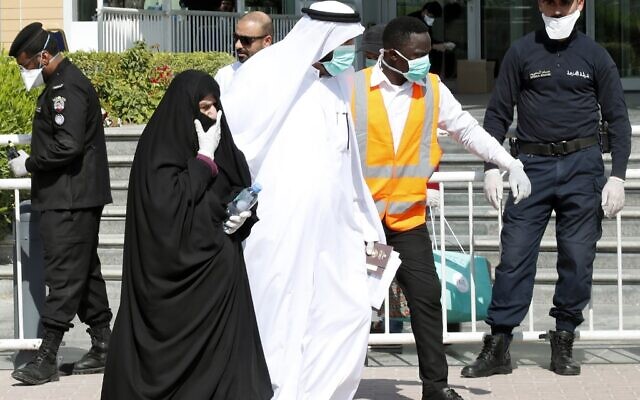 La police qatari se trouve devant un hôtel à Doha alors qu'un soignant accompagne des personnes portant des masques par crainte du coronavirus, le 12 mars 2020. (Photo par - / AFP) / Qatar OUT)