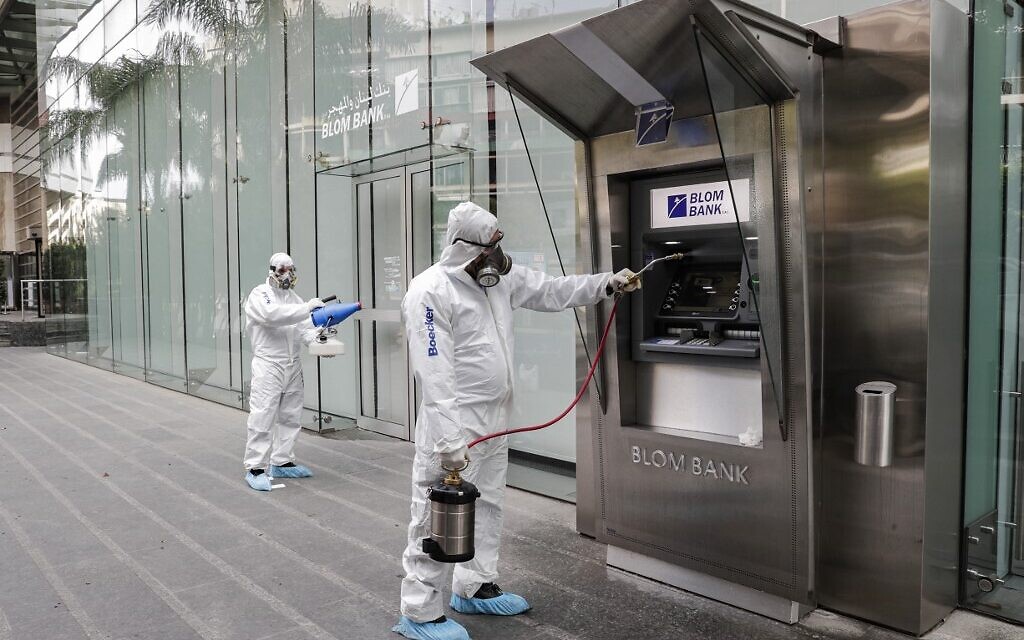 Des employés d'une société privée désinfectent un guichet de banque, 
 pour limiter la propagation du coronavirus, à Beyrouth, au Liban, le 15 mars 2020. (Crédit : ANWAR AMRO / AFP)