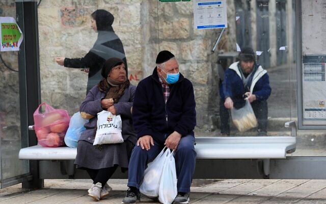 Un Israélien portant un masque attend un bus à Jérusalem le 19 mars 2020. (Crédit : EMMANUEL DUNAND / AFP)
