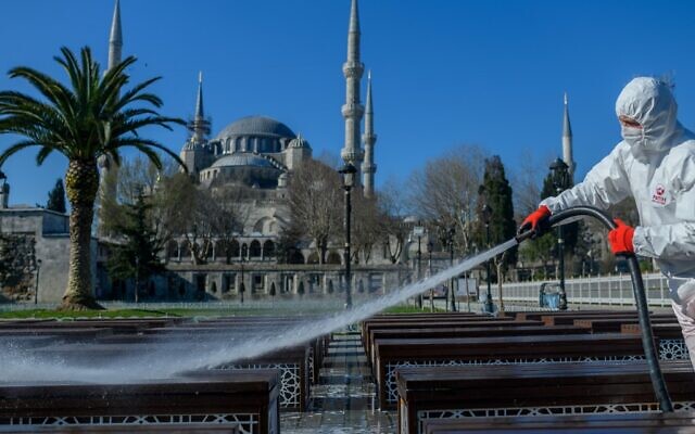 Illustration : Un employé de la municipalité de Fatih désinfecte la place Sultanhamet à Istanbul avec la mosquée Bleue à l'arrière pour prévenir la propagation du COVID-19, le 21 mars 2020 (Crédit :  BULENT KILIC / AFP)