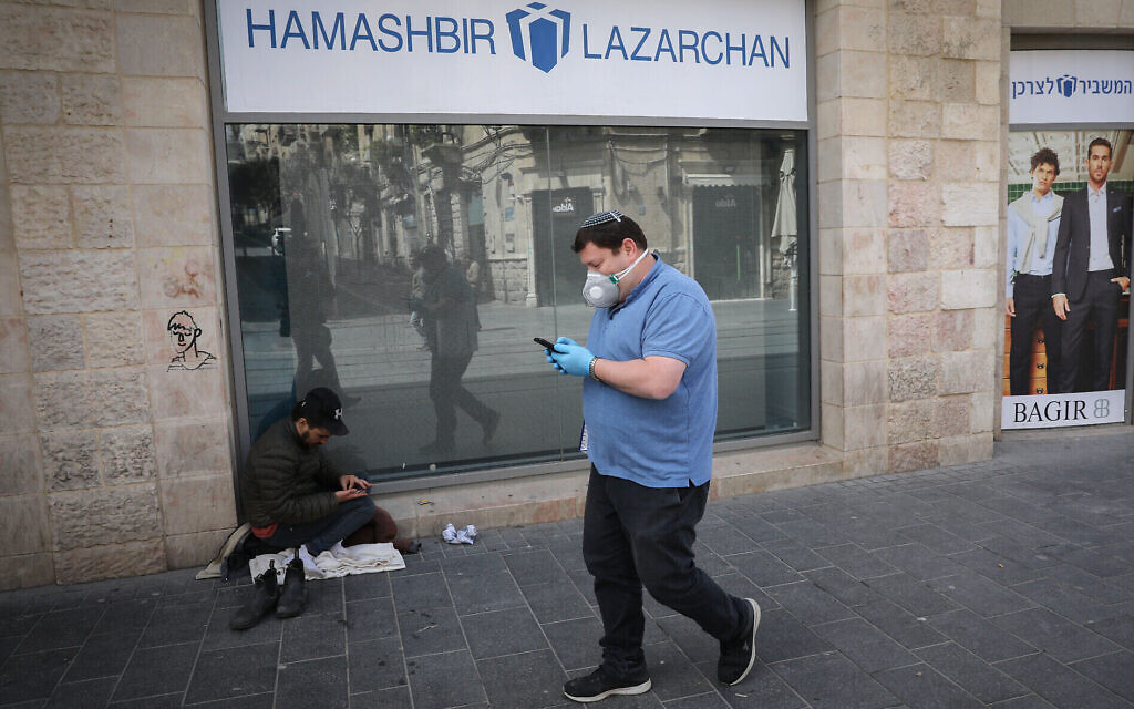 Un homme portant un masque pour se protéger du coronavirus, devant un sans-abri, près d'un centre commercial fermé à Jérusalem, le 23 mars 2020. (Crédit : Olivier Fitoussi / Flash90)