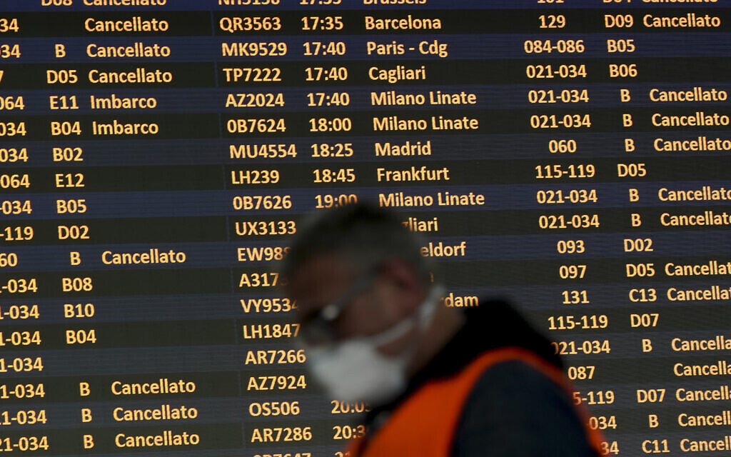 Un homme porte un masque devant un tableau des départs à l'aéroport international Leonardo da Vinci de Rome, le 12 mars 2020. (Crédit : AP Photo/Andrew Medichini)