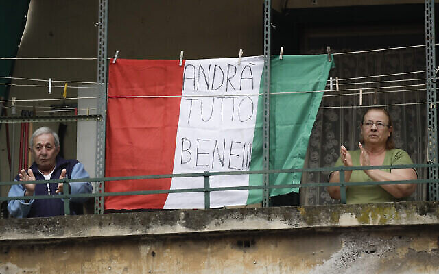 Un couple applaudit à côté d'un drapeau italien arborant le message "Tout ira bien", dans le quartier Garbatella, à Rome, le 14 mars 2020. (Crédit : AP Photo/Alessandra Tarantino)