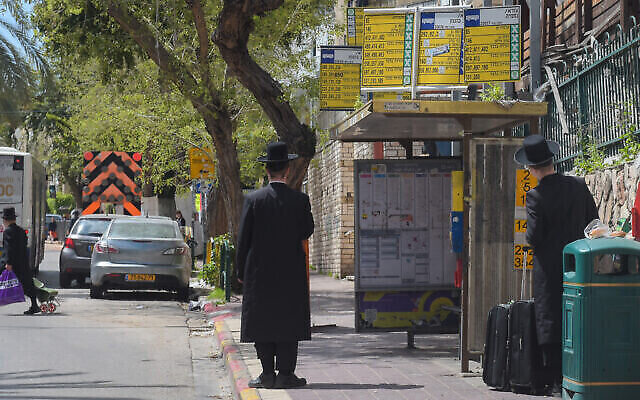 Des hommes Juifs ultra-orthodoxes attendent un bus à Bnei Brak, le 25 mars 2020. (Avshalom Sassoni/Flash90)